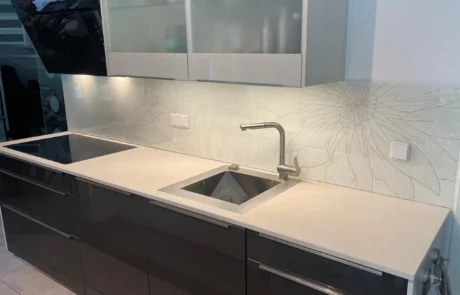 Buntentors_Glaserei_Wolff_Bremen_Kuechenrueckwaende Moderne Küchenarbeitsplatte mit Gasherd, Aufkantung aus Metall, hängendem Topflappen, Steckdosen und Oberschränken.